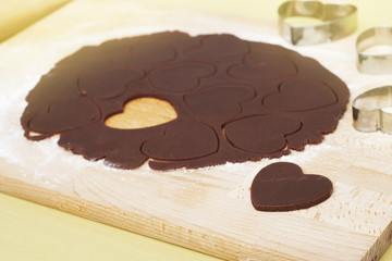Cooking process: uncooked, heart shaped cookies on baking papper, raw dough and heart shaped cookie cutter. top view.