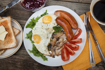 English breakfast. Eggs, sausages, mushrooms, tomatoes, toast bread. Eating tasy food over rustic wooden table.
