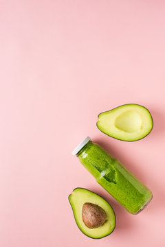 Green avocado smooothie in bottle on pink background.