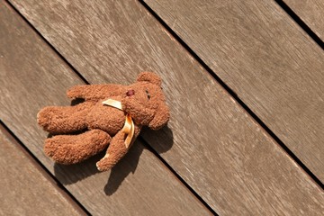 A brown teddy bear lying on a wooden surface. This image can be used to represent the concept of...