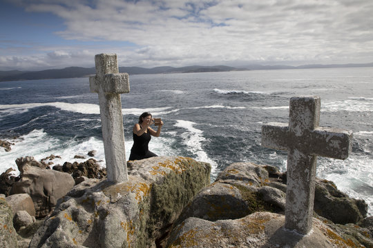 woman photographes memorial cross for lost fishermen on Cape Roncudo (Faro de Cabo Roncudo) on the coast of death (costa da more ) in  galicia, spain