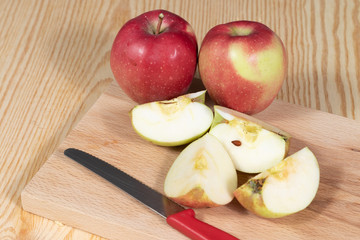 Pieces of an apple beside ripe apples and a knife
