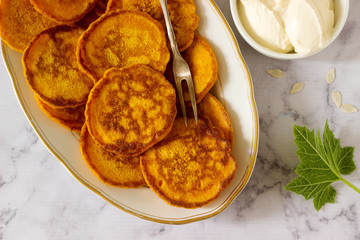 Homemade pumpkin pancakes served with sour cream on a light background.