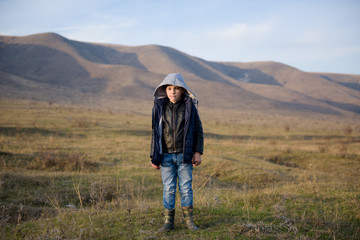 cute little boy in jacket and jeans and hood in mountains in autumn