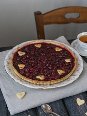cherry tart decorated with heart shape biscuits, cup of tea, vintage chair, on old wooden backdrop in rustic style