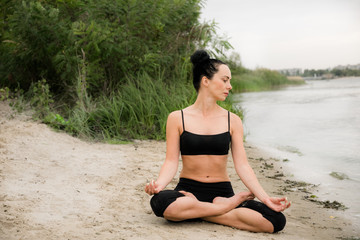 Fototapeta na wymiar Young woman doing yoga on the river bank. City break