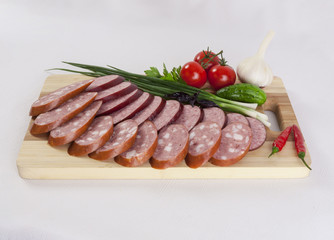 still life with sliced smoked sausage greens and tomatoes on a white background