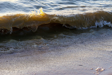 Waves on the sandy shore of a large river. The rays of light are reflected in the waves.