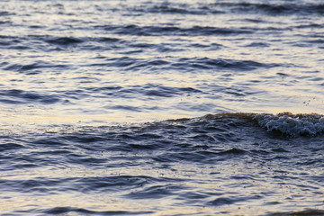 Waves on the sandy shore of a large river. The rays of light are reflected in the waves.