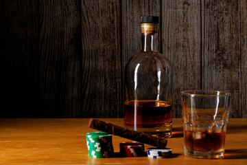 Obraz na płótnie Canvas Cuban cigar based on poker chips. Whiskey bottle and glass with cubed ice on a wooden background