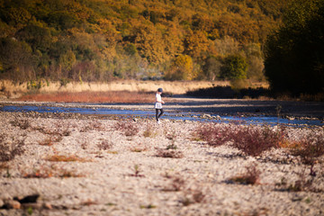 Little blonde girl on the riverside. Autumn in the yellow forest