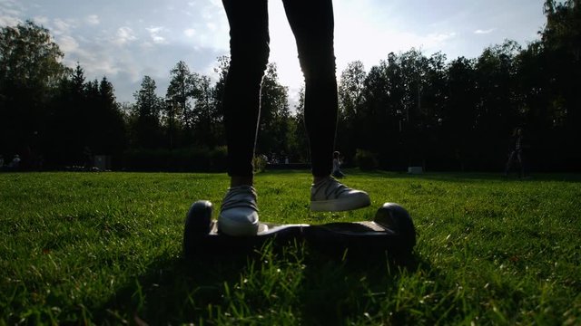 A girl with a beautiful slender figure riding a gyro on the grass in the park in the summer. The sun is shining.