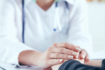 Friendly female doctor's hands holding female patient's hand for encouragement and empathy...