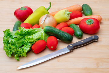 Vegetables on wooden cutting board. Vegetables: lettuce, onions, tomatoes, cucumbers, onions, carrots, red sweet peppers.