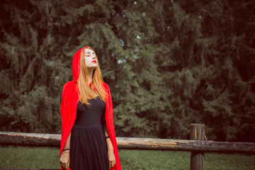 Obraz premium Concept of Halloween. Beautiful and simple costume of little red hood. Mysterious hooded figure in misty forest. Girl in red raincoat. Cosplay Fairy Tale Little Red Riding Hood 