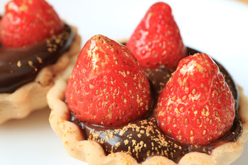 Close-up of chocolate tart topped with fresh strawberries and edible gold powder served on white plate 