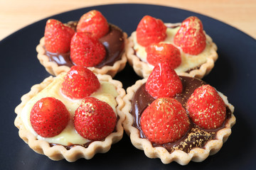 Many of mini chocolate tarts topped with fresh strawberries and edible gold powder served on black plate 