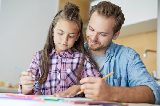 Cute girl drawing and looking at paper sheet with picture while her dad helping to get and idea