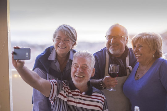 group of people senior adults caucasian having fun celebrating together outdoor at home in the terrace with rooftop view. taking picture selfie with phone technology smiling and laughing with joy. 