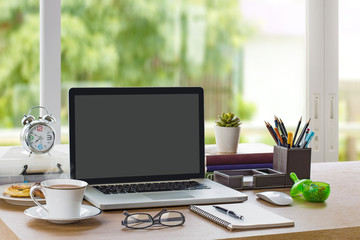 Home office workplace with mockup laptop (with blank screen for montage), notebook, tea cup, clock and stationery on wooden desk. Good morning, Fresh start, Start up or Start working concept.
