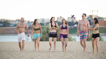 Beautiful young sports men and women walking on the beach after a game of volleyball, talking, smiling. Girl threw the ball.