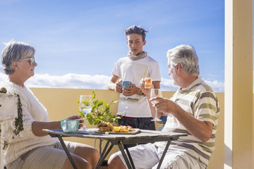 grandfathers adult mature and teenager nephew enjoy outdoor in the terrace some leisure with food and drinks. ocean and city view, vacation sunny day nice weather concept and background. happy people 