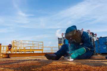 Industrial welder worker holding welding torch during perform welding sheet metal steel plate in construction factory by wearing heat protection gloves with smoke, spark, arc, fire, flash, hot