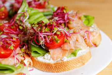 Fresh homemade small sandwiches with sprouts, smoked salmon, bread, lettuce, smoked salmon, coctail tomato, and white cheese prepared to house party