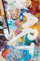 Paintbrush of artist on palette with mixture of various colors and white word art