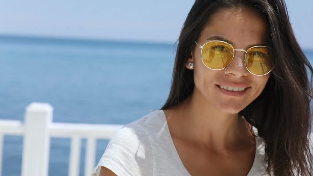Happy smiling young brunette woman in trendy sunglasses turning to camera, leading to the seaside. Follow me concept, positive day, good emotions. Female portrait