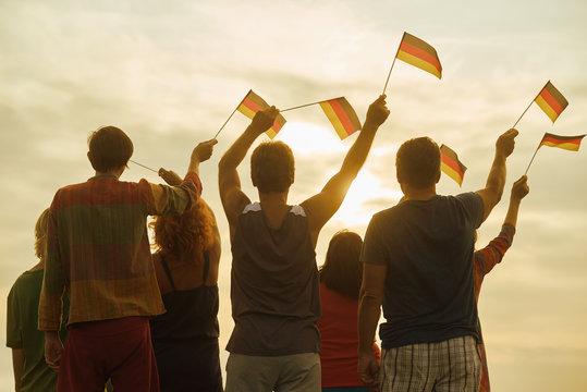 Young people waving deutsch flags, back view. People with deutsch flags silhouette, down sky background.
