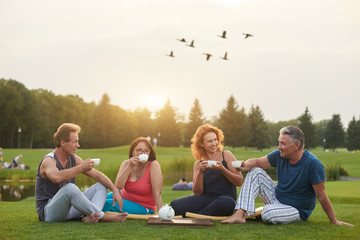 Friendly mature adult people drinking tea. Friends sitting outdoor in the park at the evening.