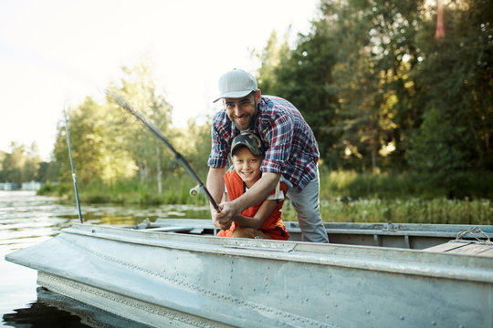Happy father and son holding rod while sitting in boat and fishing in natural environment