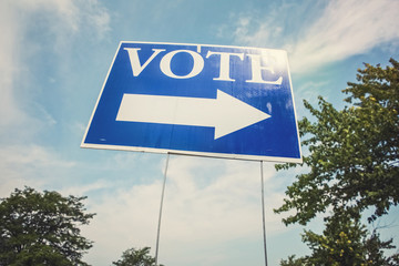 Vote sign with arrow  against the sky with sun flare