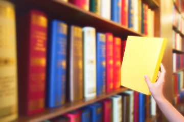 Women hand pulling yellow book from wood bookshelves in public library. Colorful books, Textbook, Literatur on bookshelf.