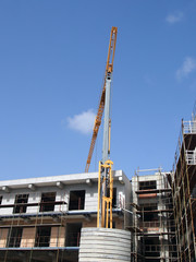 Fototapeta premium A yellow construction crane working on a modern concrete apartment development with scaffolding with blue sky and sunlight