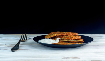 potato pancakes with sour cream, on a black plate on a wooden background. Home kitchen.