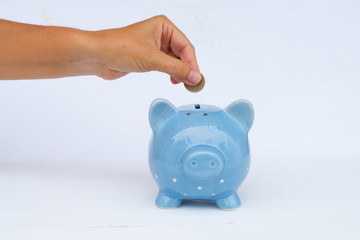 Someones hand putting coin into piggy bank on white background, savings concept