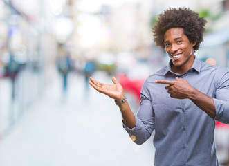 Afro american man over isolated background amazed and smiling to the camera while presenting with hand and pointing with finger.