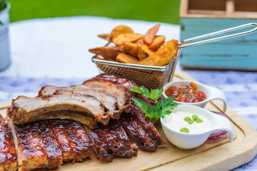 gegrillte Marinierte Spare Ribs mit Country Farmer Potaoes Kartoffeln auf einem Holzbrett mit Dips