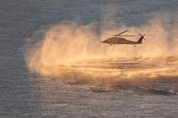 Helicopter in plumes of water vapor and drizzle at sunset. Mock up rescue mission above the...