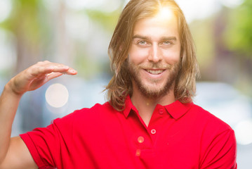 Young handsome man with long hair over isolated background gesturing with hands showing big and large size sign, measure symbol. Smiling looking at the camera. Measuring concept.