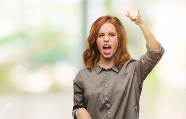 Young beautiful woman over isolated background angry and mad raising fist frustrated and furious...