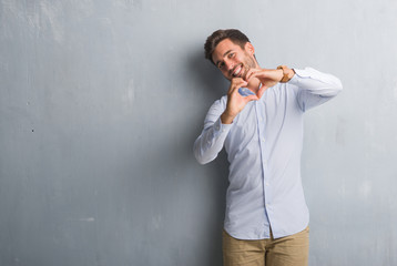 Handsome young business man over grey grunge wall wearing elegant shirt smiling in love showing heart symbol and shape with hands. Romantic concept.
