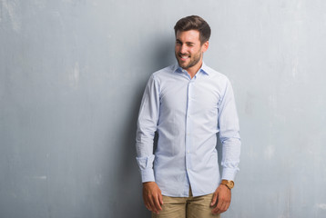 Handsome young business man over grey grunge wall wearing elegant shirt winking looking at the camera with sexy expression, cheerful and happy face.