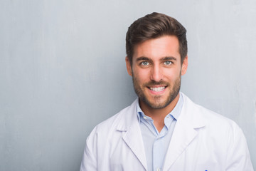 Handsome young professional man over grey grunge wall wearing white coat with a happy and cool smile on face. Lucky person.