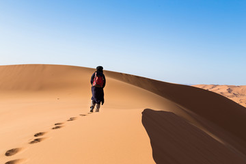 Fototapeta na wymiar One male tuareg climbing a dune in the desert.
