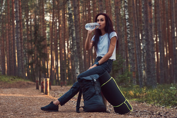 Tourist girl stopped to rest and drink water in the beautiful autumn forest.