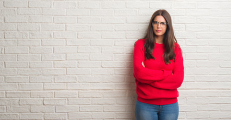Obraz na płótnie Canvas Young brunette woman standing over white brick wall skeptic and nervous, disapproving expression on face with crossed arms. Negative person.