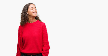 Young hispanic woman wearing red sweater looking away to side with smile on face, natural expression. Laughing confident.